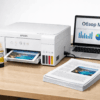 Многофункциональный принтер Epson EcoTank L3210 с бутылочками чернил на столе рядом с ноутбуком.